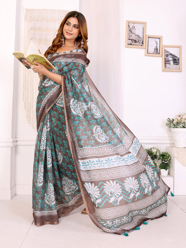Woman wearing a patterned saree holding a book in a bright room.